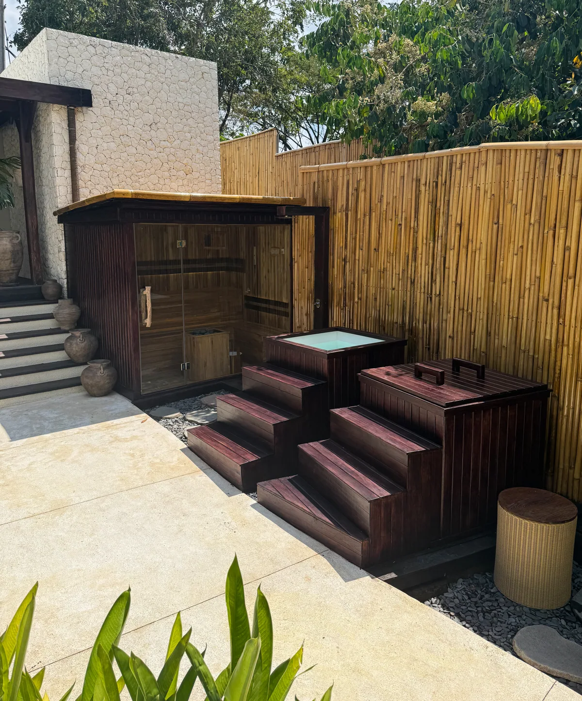 A handcrafted wooden sauna and two ice baths installed in a tropical outdoor space